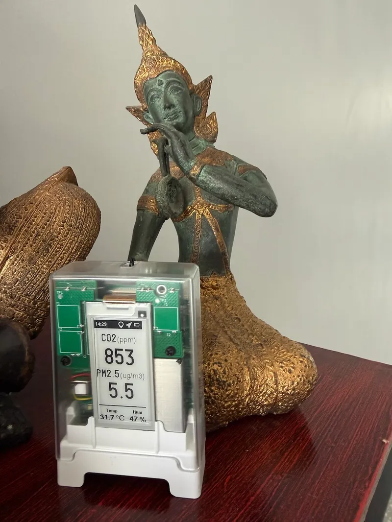 Portable air quality monitor on a table beside a Thai-style statue